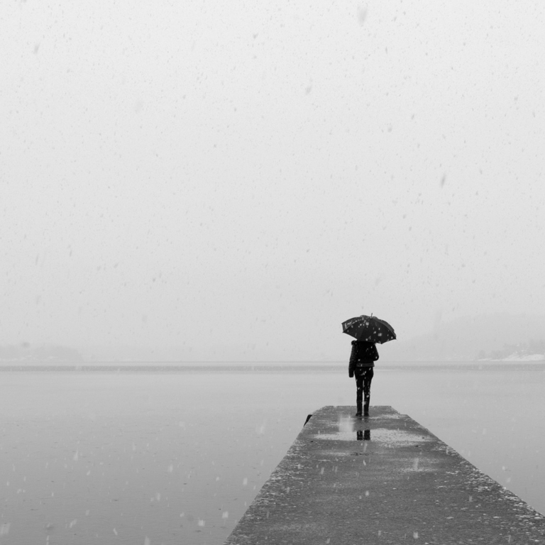 Person standing at the end of a dock with an umbrella